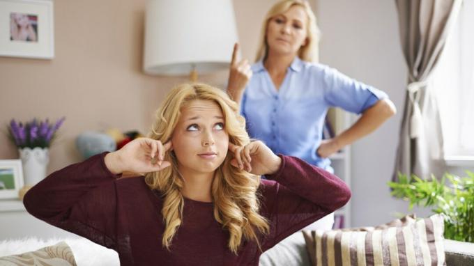 Menina adolescente desafiadora cobre as orelhas com os dedos no quarto, enquanto a mãe a repreende