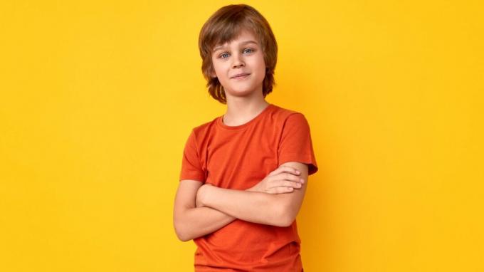 Garoto pré-adolescente positivo em roupa casual com os braços cruzados e olhando para a câmera contra um fundo amarelo vivo