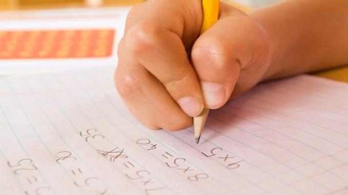 A mão de uma criança que completa uma tarefa de casa com a ajuda de acomodações matemáticas